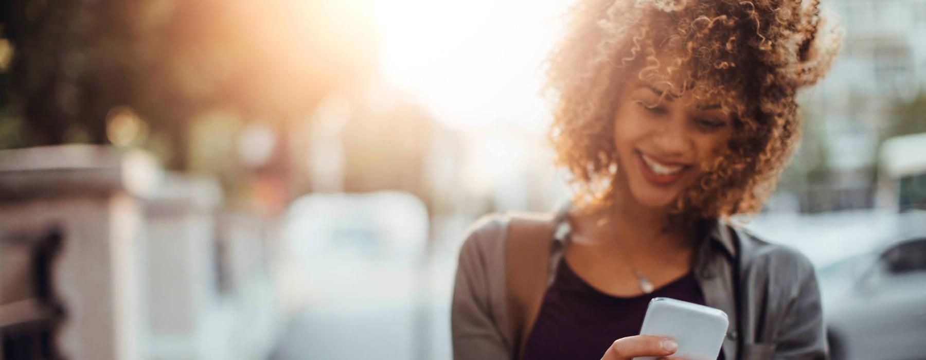 woman texts on her phone as she walks through the city