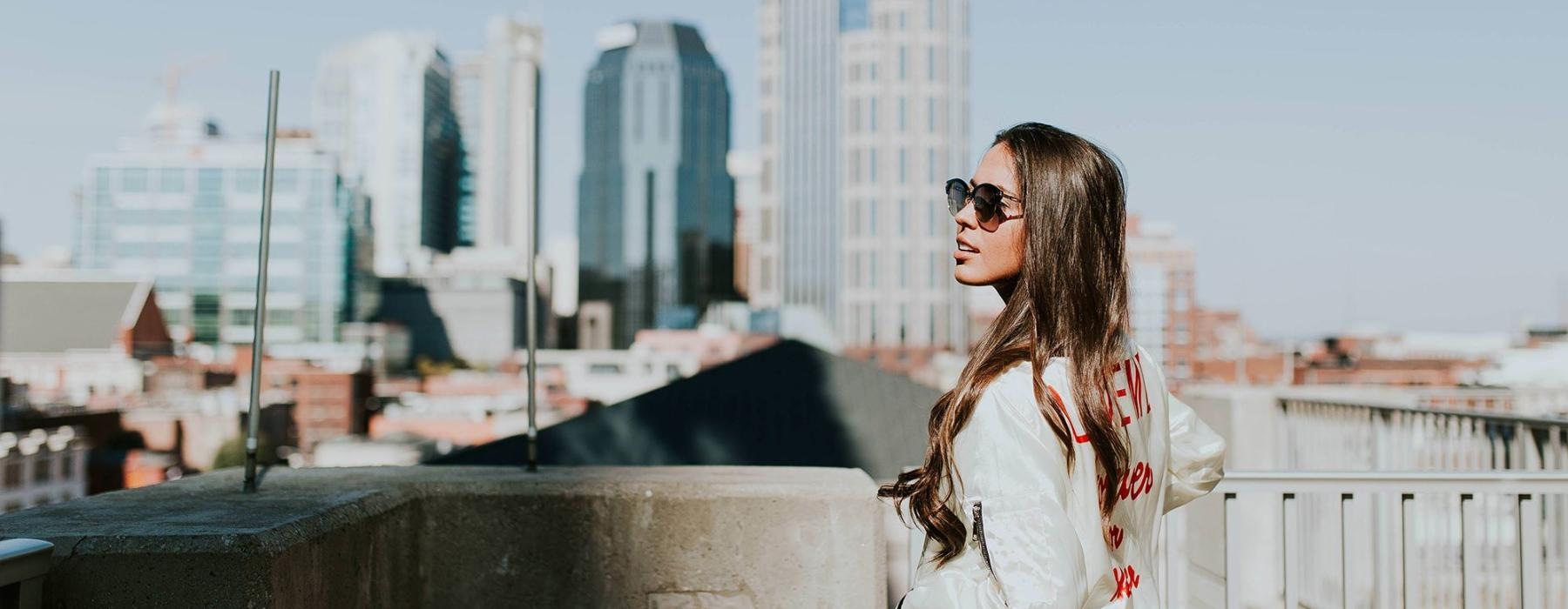 woman with sunglasses stands on a rooftop overlooking the city